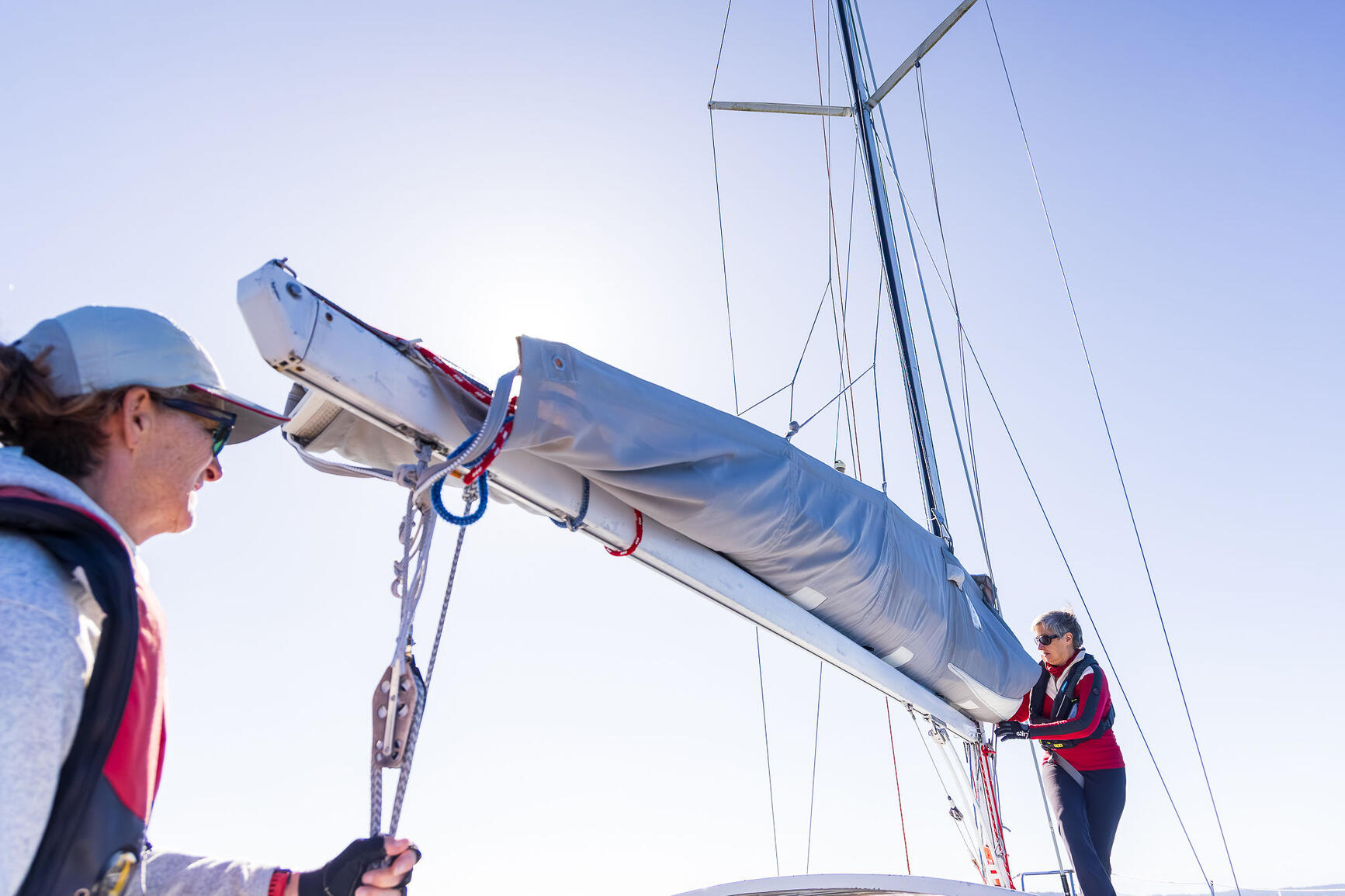 Furling sails. Two women learning to sail together on deck, handling the boom and furled sails during a women's sailing lesson in BC.